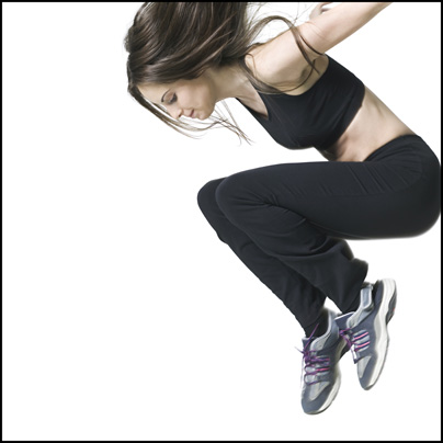 medium shot of a young adult woman in a black exercise outfit as she jumps up
